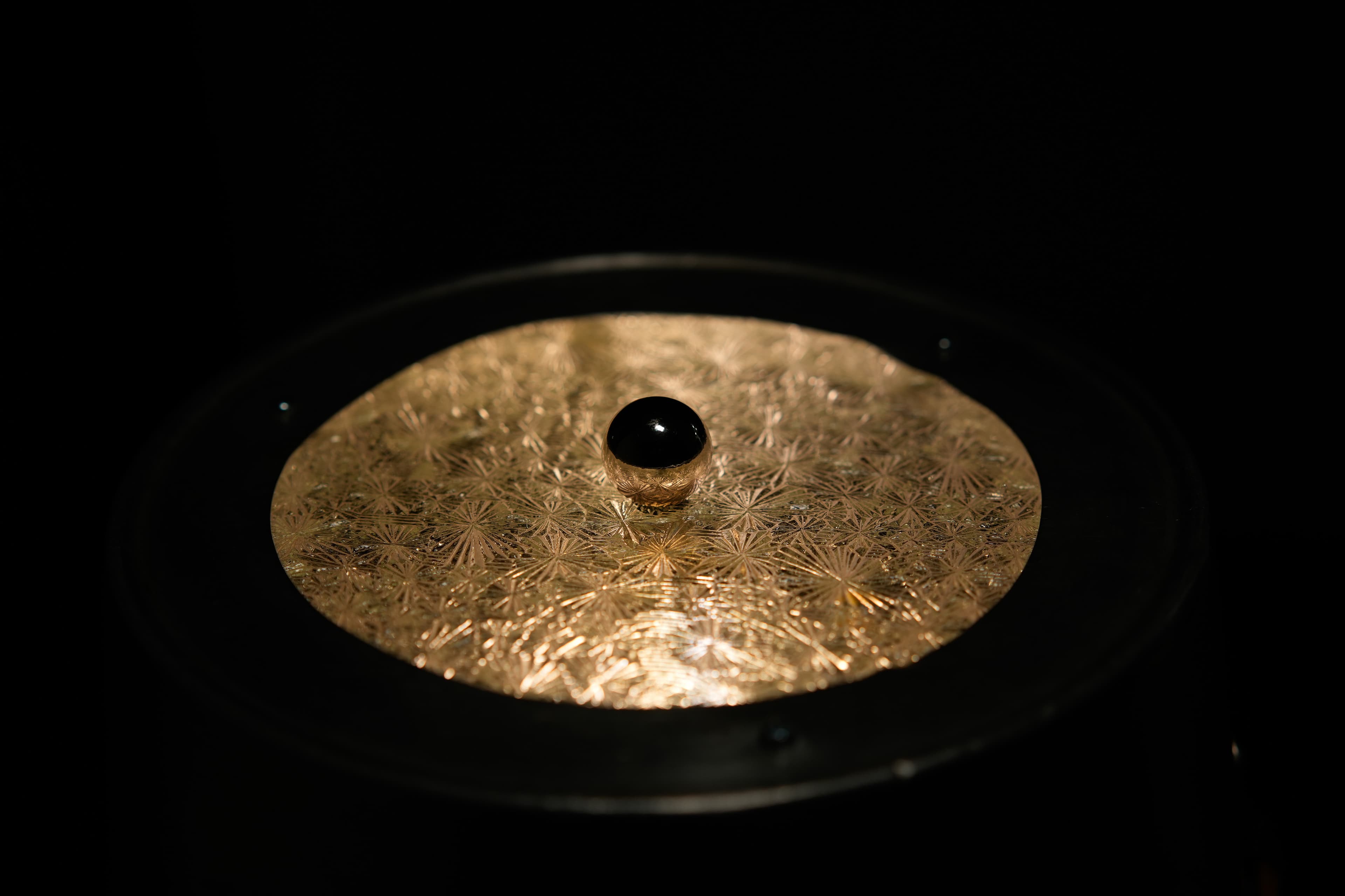 Circular gold sculptural disc with a black sphere at center